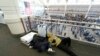 Dua orang pelancong tidur di bandara sementara para pelancong lainnya antre melewati pos pemeriksaan keamanan di Bandara Internasional Denver saat badai musim dingin melanda AS, 23 Desember 2022.