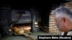 Pembuat roti Prancis Franck Burgaud mengeluarkan nampan roti dari oven berbahan bakar kayu di toko roti "Au veritable four a bois" di Challans, Prancis, 5 Januari 2023. (Foto: REUTERS/Stephane Mahe)