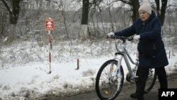 Una mujer empuja su bicicleta por una carretera más allá de un cartel que dice "Stop-Mines" cerca del pueblo de Makariv, al oeste de Kiev, el 22 de noviembre de 2022, en medio de la invasión rusa de Ucrania.