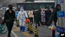 A worker in a protective suit sprays disinfectant as residents stand in line for routine COVID-19 tests in Beijing, Nov. 24, 2022. Citizens have shown increasing frustration with repeated lockdowns and testing for the disease.