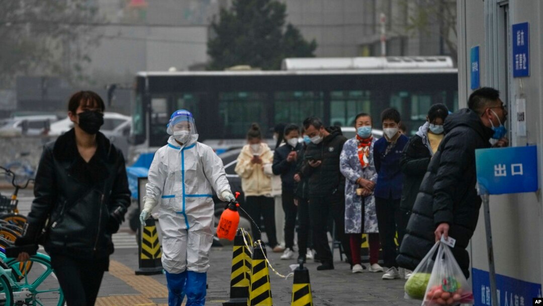A worker in a protective suit sprays disinfectant as residents stand in line for routine COVID-19 tests in Beijing, Nov. 24, 2022. 