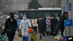 A worker in a protective suit sprays disinfectant as residents stand in line for routine COVID-19 tests in Beijing, Nov. 24, 2022. 