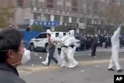 In this photo provided Nov 23, 2022, security personnel in protective clothing were seen taking away a person during protest at the factory compound operated by Foxconn Technology Group who runs the world's biggest Apple iPhone factory in Zhengzhou in central China's Henan province.