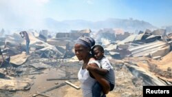 A woman and a child look at the destruction as a blaze destroyed many shacks in Masiphumelele township in Cape Town, South Africa, November 21, 2022.