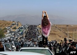 Seorang perempuan tak berjilbab berdiri di atas sebuah kendaraan ketika ribuan orang berjalan menuju pemakaman Aichi di Saqez, kota asal Mahsa Amini di Provinsi Kurdistan, Iran barat. (Foto: AFP)