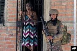 FILE - A resident looks out from her doorway as a soldier takes part in an operation in search of gang members, in Soyapango, El Salvador, Dec. 3, 2022.