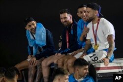 Kapten Lionel Messi (dua dari kiri), duduk bersama Angel de Maria (kedua dari kanan) dan Nicolas Otamendi (kanan), di atas bus yang membawa para pemain dari tim sepak bola Argentina setibanya di bandara Ezeiza, pinggiran kota Buenos Aires, Argentina, Selasa, 20 Desember 2022. (AP Photo/Rodrigo Abd)