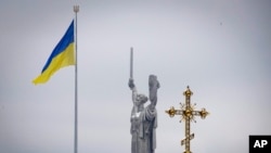 A cross of the Pechersk Lavra monastic complex is seen against background of the Ukrainian national flag and the Motherland Monument in Kyiv, Ukraine, Nov. 22, 2022.