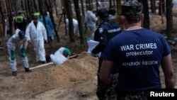 Seorang jaksa kejahatan perang berdiri di dekat para ahli yang tengah menggali kuburan para korban invasi Rusia di Kota Izium, Kharkiv, Ukraina, pada 18 September 2022. (Foto: Reuters/Umit Bektas)