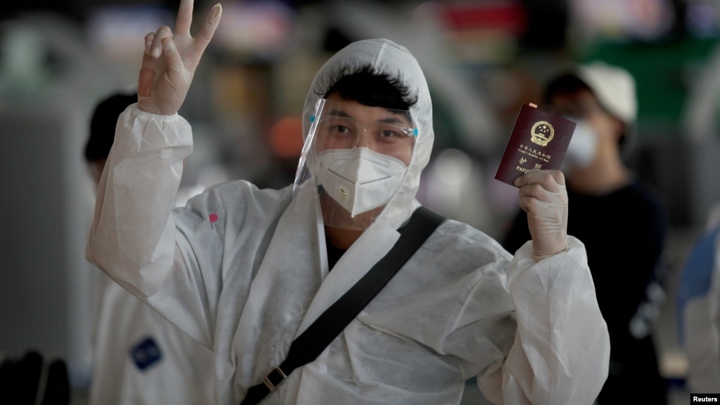 资料照：通过曼谷机场内一名身穿防护服的中国学生举起中国护照。（2020年4月21日）(photo:VOA)