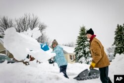 Marissa dan Mark Kallevig menyekop salju dari trotoar di rumah depan mereka, di Duluth, Minnessota, Kamis, 15 Desember 2022.(AP Photo/Holden Law)