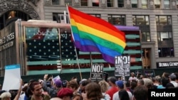 26일 도널드 트럼프 대통령의 성전환자 군복무 금지 방침이 알려진 직후, 이에 항의하는 시민들이 성소수자 권리를 상징하는 무지개색 깃발을 들고 뉴욕 타임스스퀘어에서 시위하고 있다.