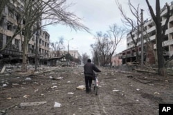 Čovek vozi bicikl ulicom između teško oštećenih zgrada nakon ruskog bombardovanja Mariupolja, 10. marta 2022. (AP Photo/Evgeniy Maloletka)