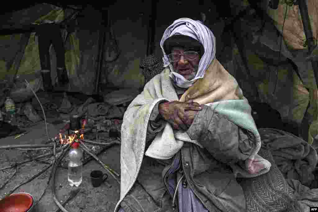 Palestinian Mohammad al-Malalha warms himself with a blanket following rain in Rafah in the southern Gaza Strip, March 13, 2022. (Photo by SAID KHATIB / AFP)