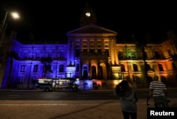 FILE - People look on as the city hall is lit up in the colors of the Ukrainian flag in support of Ukrainians following Russia's invasion of Ukraine, at the Cape Town city hall, in Cape Town, South Africa, March 2, 2022.