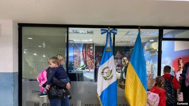 Una mujer ucraniana, con su hijo en brazos, aguarda mientras tramita su entrada al país, en el Aeropuerto Internacional La Aurora, en Ciudad de Guatemala, en la noche del 11 de marzo de 2022. [Foto: Cortesía del Instituto Guatemalteco de Migración]