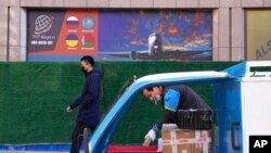 FILE - A deliveryman prepares packages as another man walks past an advertisement for cargo services at a trading center in Beijing, Feb. 26, 2022.