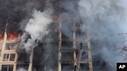 Petugas pemadam kebakaran bekerja di sebuah gedung apartemen yang rusak akibat penembakan di Kyiv, Ukraina, Selasa, 15 Maret 2022. (Foto: AP/Efrem Lukatsky)