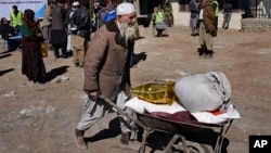 FILE - An Afghan man carries food supplies in a wheelbarrow during a distribution of humanitarian aid for families in need, in Kabul, Afghanistan, Feb. 16, 2022. 