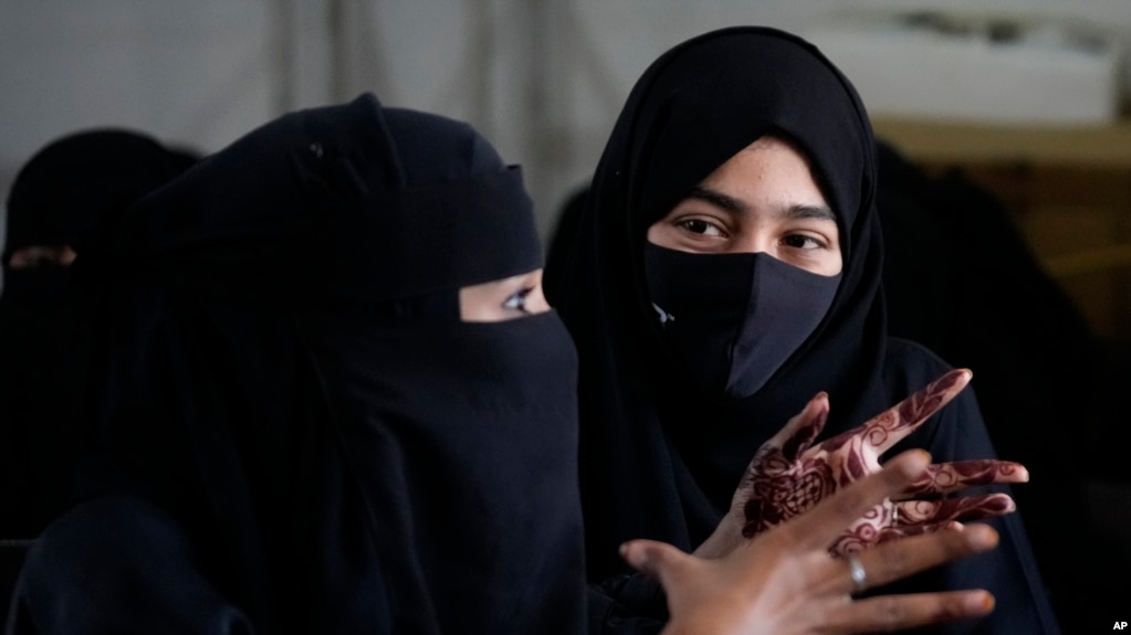 A veiled Indian Muslim student, her hands decorated with henna, talks to her friend as they gather to meet student activists in Kundapur in district Udupi, Karnataka state, India, Saturday, Feb. 26, 2022. (AP Photo/Aijaz Rahi)