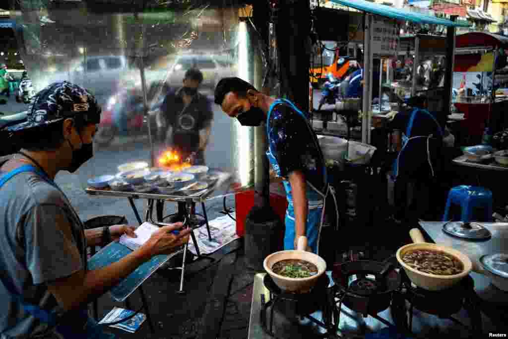 People wearing face masks as protection against COVID-19 sell street food in Bangkok&#39;s Chinatown, Thailand.