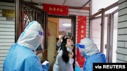 Petugas yang mengenakan pakaian pelindung tampak melakukan tes usap pada seorang warga di sebuah kompler perumahan di Shenzhen, Provinsi Guangdong, China, pada 14 Maret 2022. (Foto: cnsphoto via Reuters) 
