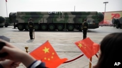 Para penonton mengibarkan bendera China ketika kendaraan militer yang membawa rudal balistik DF-41 bergerak dalam parade militer di Beijing pada 1 Oktober 2019. (Foto: AP/Mark Schiefelbein)