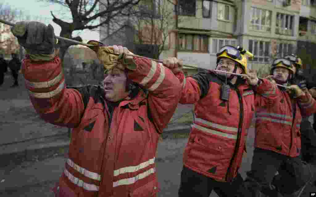 Los bomberos tiran de una cuerda para dirigir la caída de un árbol mientras trabajan para extinguir un incendio en un edificio de apartamentos destruido después de un bombardeo en una zona residencial en Kiev, Ucrania.