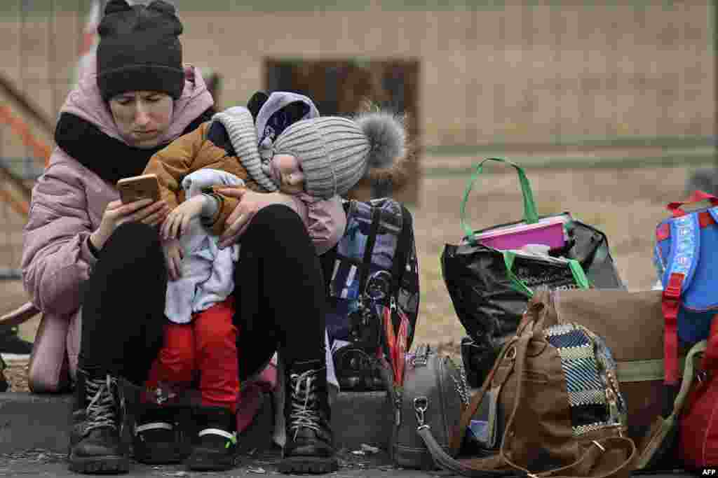 A woman with her child checks her mobile phone as she waits for relocation outside the main shelter and relocation center in Przemysl, southeastern Poland. More than 3 million people have fled Ukraine since the start of the invasion, the U.N. migration agency IOM said.