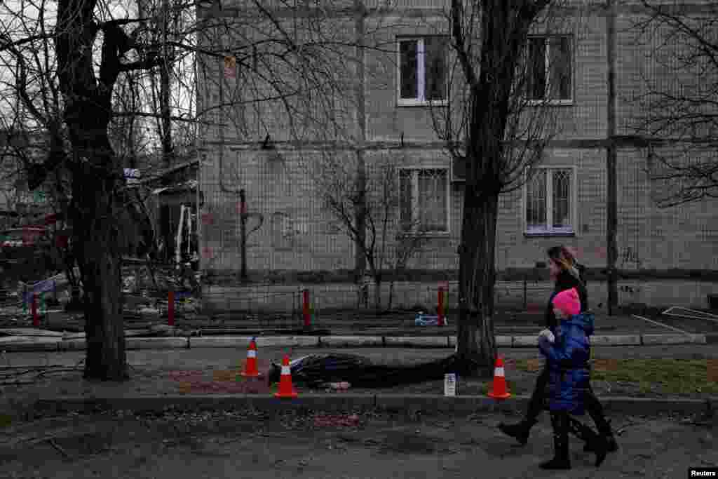 A woman and a child walk past a dead body in front of a residential building that was hit by Russian shelling in the Obolon district in Kyiv, Ukraine.