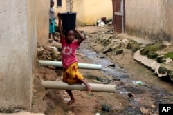 FILE - A girl carrying water on her head walks past sewage around houses in Abuja, Nigeria, Sept. 3, 2021.