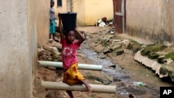 A girl carrying water on her head walks past sewage around houses in Abuja, Nigeria, Sept. 3, 2021. 