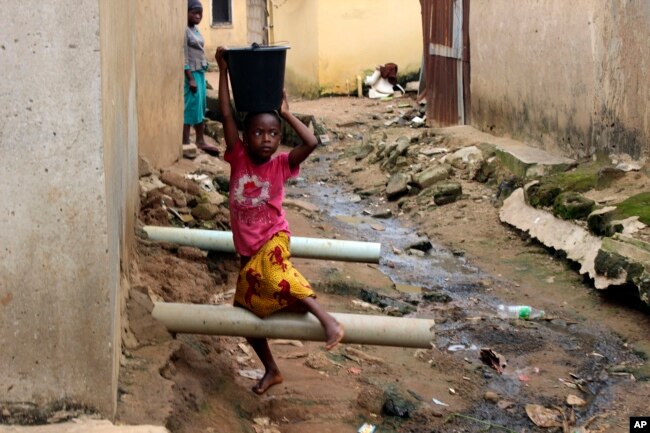 FILE - A girl carrying water on her head walks past sewage around houses in Abuja, Nigeria, Sept. 3, 2021.