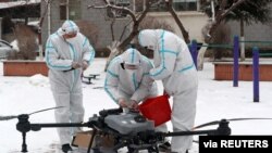 Trabajadores con trajes protectores preparan un dron en medio de la nieve para desinfectar un complejo residencial bajo aislamiento, luego del brote de COVID-19 en Changchun, provincia de Jilin, China, el 14 de marzo de 2022. 