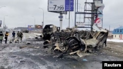 FILE - People walk past a destroyed vehicle on a road, amid Russia' ongoing invasion of Ukraine, in Bucha, Ukraine, March 2, 2022 in this still image taken from video.