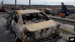 রাশিয়ার হামলায় পুড়ে যাওয়া একটি গাড়ির পাশ দিয়ে হেঁটে যাচ্ছেন ইউক্রেনের ইরপিনের একজন নাগরিক। মার্চ ১২ ২০২২। (ছবি- এপি) 