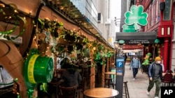 FILE - Pedestrians pass outside the sparsely populated sidewalk dining area beside the Playwright Celtic Pub on Saint Patrick's Day in midtown Manhattan, March 17, 2021, New York.