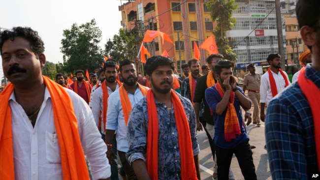 India's Hindu right wing Bajrang Dal activists donning saffron scarves and waving saffron flags demand a probe in the recent killing of one of their associates in Karnataka's Shivamogga district, during a protest rally in Udupi, Karnataka, India, Feb. 23,