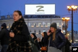 People walk past the letter Z, which has become a symbol of the Russian military, and a hashtag reading "We don't abandon our own" on an advertisement screen in St. Petersburg, Russia, March 9, 2022.