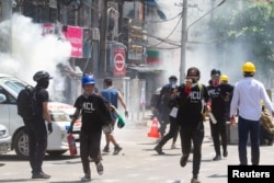 FILE - Tear gas and fire extinguisher gas float around demonstrators as they run away from police during a protest against the military coup in Yangon, Myanmar, March 8, 2021.