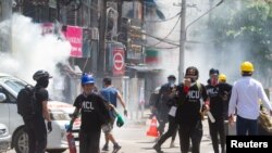 FILE - Tear gas and fire extinguisher gas float around demonstrators as they run away from police during a protest against the military coup in Yangon, Myanmar, March 8, 2021.