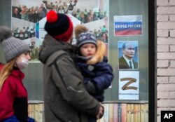 FILE - A family walk past a portrait of Russian President Vladimir Putin, a sign reading 'Go Russia!' and the letter Z, which has become a symbol of the Russian military, displayed in the window of a children's library in St. Petersburg, March 11, 2022.