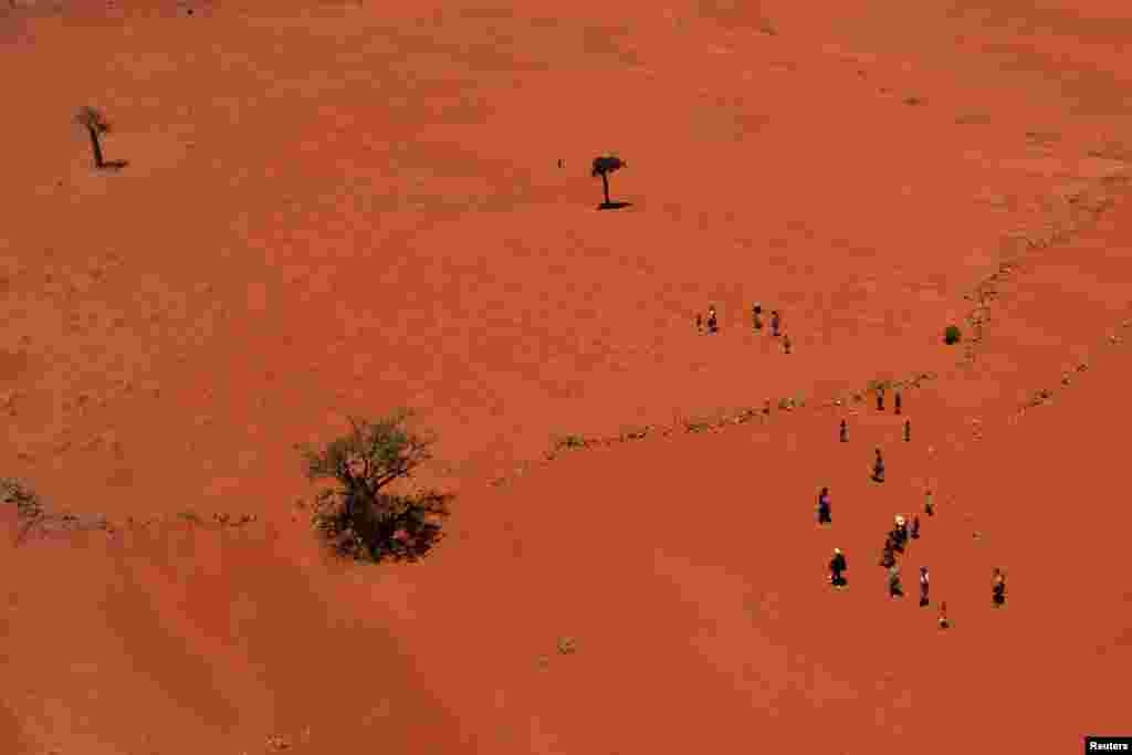 Locals walk through a field covered with red sand in Anjeky Beanatara, Androy region, Madagascar.