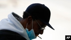 FILE - A man with a protective mask smokes a cigarette in Detroit, April 8, 2020. US cigarette smoking dropped to a new all-time low in 2020, according to data released by the Centers for Disease Control and Prevention.