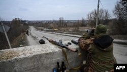 Un militaire ukrainien regarde à travers des jumelles vers la ville de Stoyanka à un point de contrôle avant le dernier pont sur la route qui relie Stoyanka à Kiev, le 6 mars 2022.