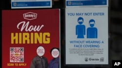 FILE - A hiring sign is posted next to a COVID-19 warning at a now closed Denny's restaurant downtown Los Angeles, March 15, 2022. 