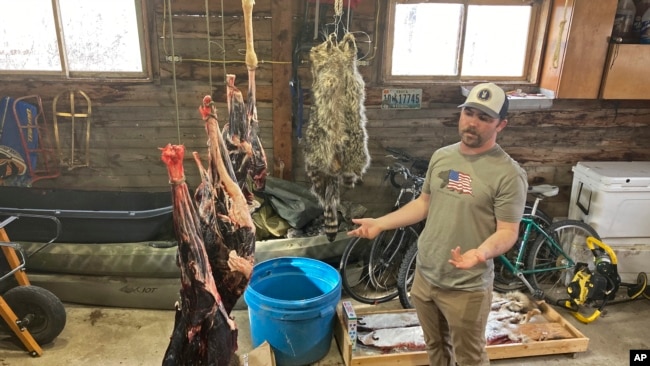 Jaden Bales stands near mule deer meat hanging in his garage Thursday, March 3, 2022, south of Lander, Wyoming. (AP Photo/Mead Gruver)