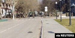 资料照片：社交媒体直播画面截图显示，人们在赫尔松抗议俄军入侵，较远处是俄军士兵及标有Z字符号的军车。(2022年3月13日)