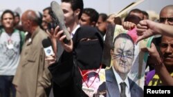 Una mujer sostiene un zapato y un manchado retrato del ex presidente egipcio Hosni Mubarak, que fue condenado este sábado 2 de junio a cadena perpetua.