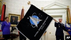 Secretary of the Air Force Barbara Barrett, left, watches Chief Master Sgt. Roger Towberman hold the United States Space Force flag as it is presented in the Oval Office of the White House, May 15, 2020, in Washington.